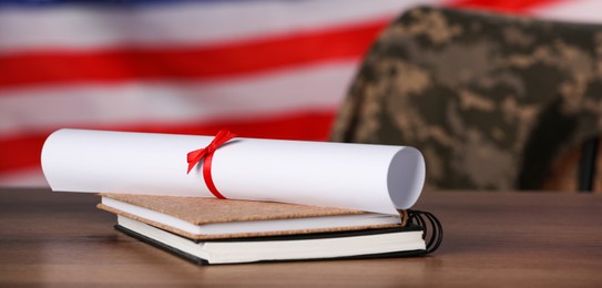 Image of Military education. Diploma and notebooks on wooden table against flag of USA. Chair with soldier's jacket indoors