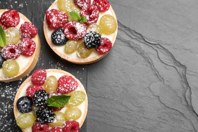 Delicious tartlets with berries on black table, top view. Space for text