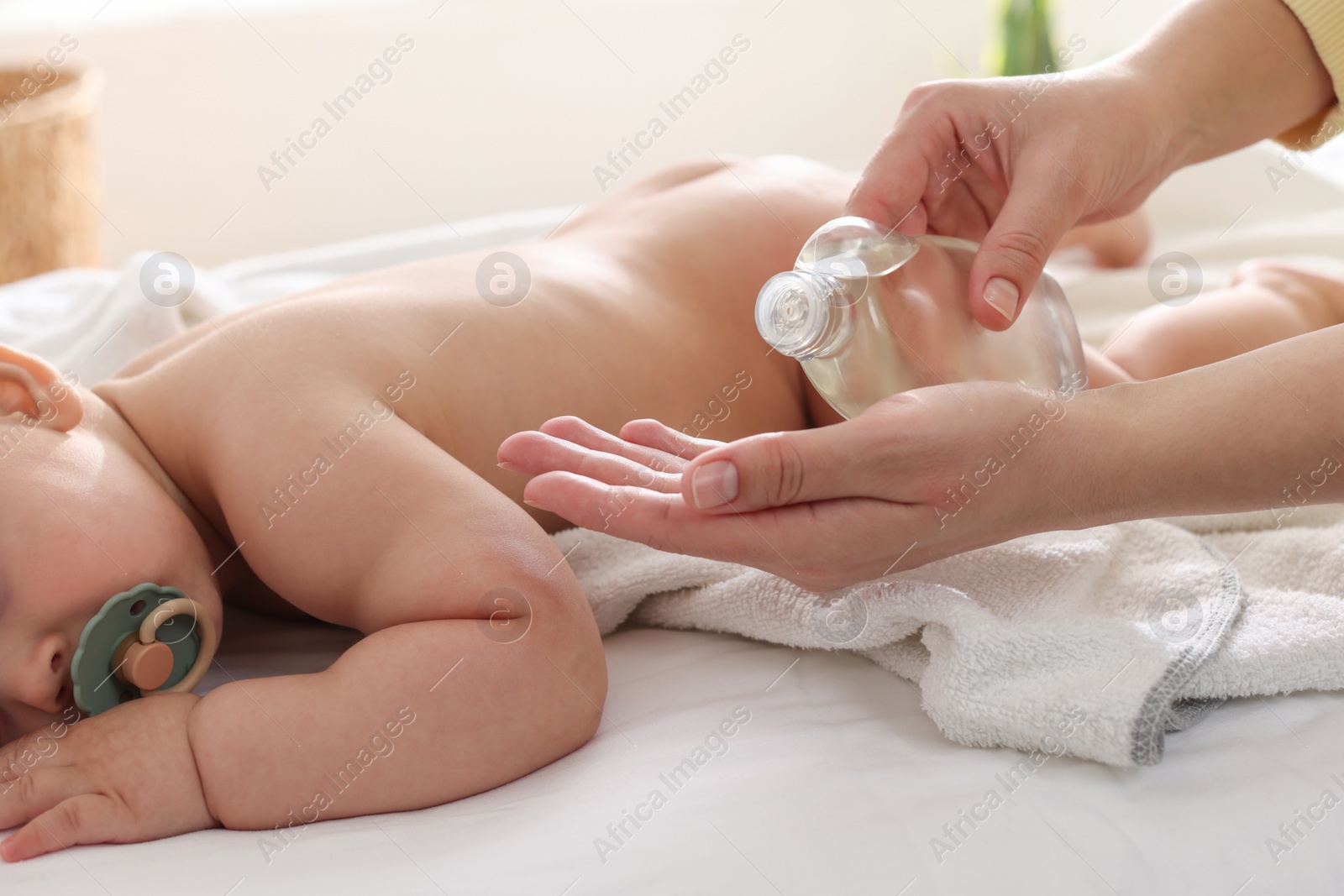 Photo of Mother with bottle of massage oil near baby on bed at home, closeup