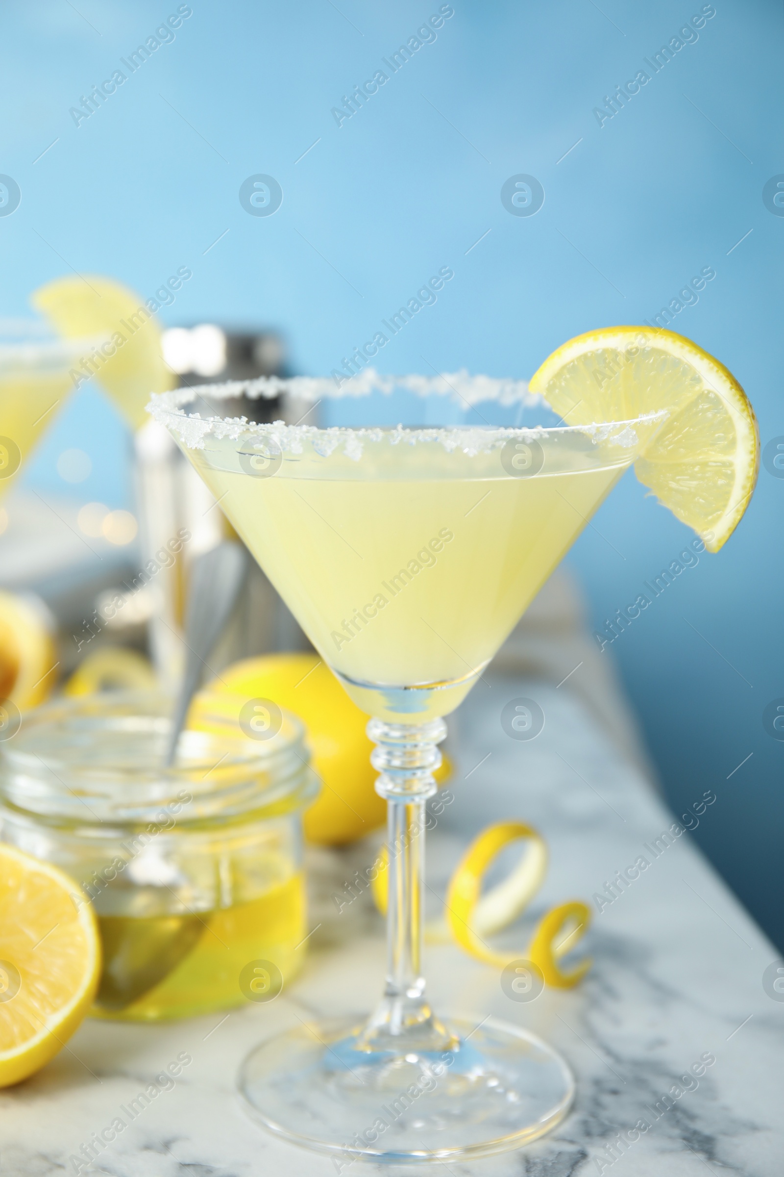 Photo of Delicious bee's knees cocktail and ingredients on white marble table against light blue background