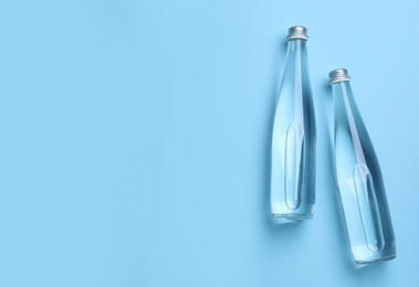 Glass bottles with water on light blue background, flat lay. Space for text