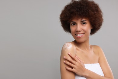 Photo of Beautiful young woman applying body cream onto shoulder on grey background, space for text