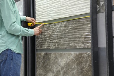 Photo of Man using tape measure while choosing tile in store, closeup