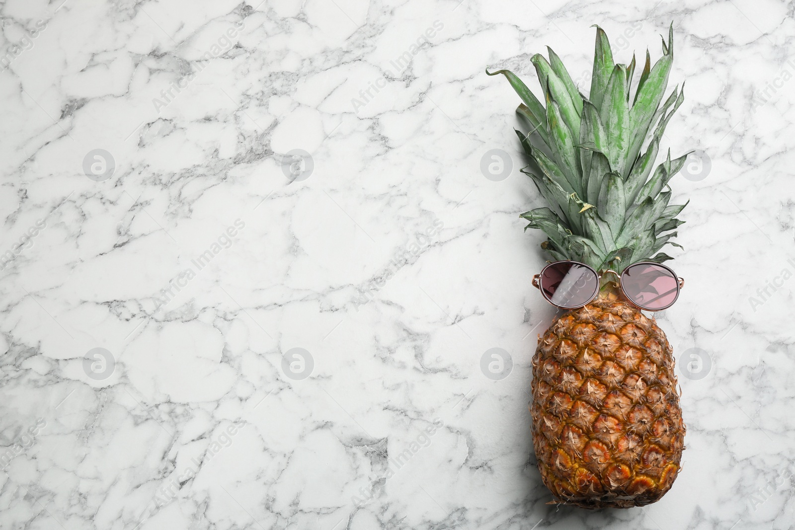 Photo of Top view of pineapple with sunglasses on white marble background, space for text. Creative concept