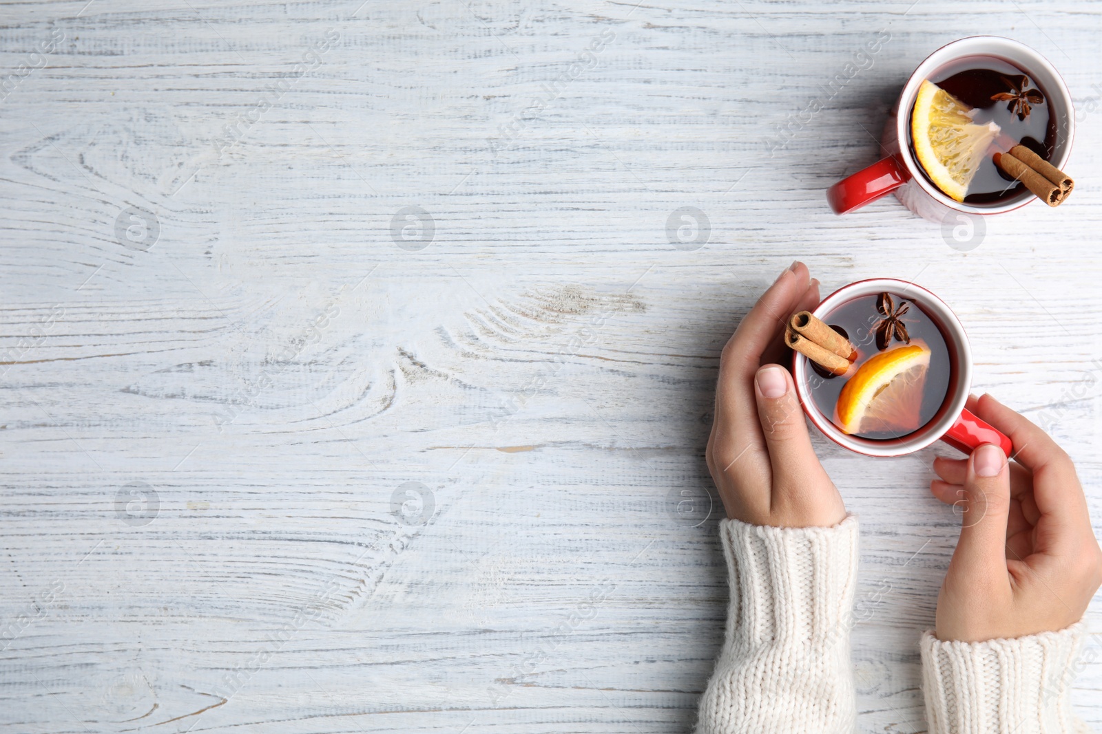 Photo of Woman with cups of hot winter drink at white wooden table, top view. Space for text