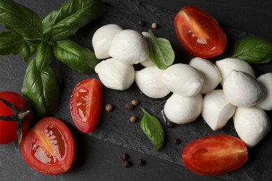 Delicious mozzarella balls, tomatoes and basil leaves on black table, flat lay
