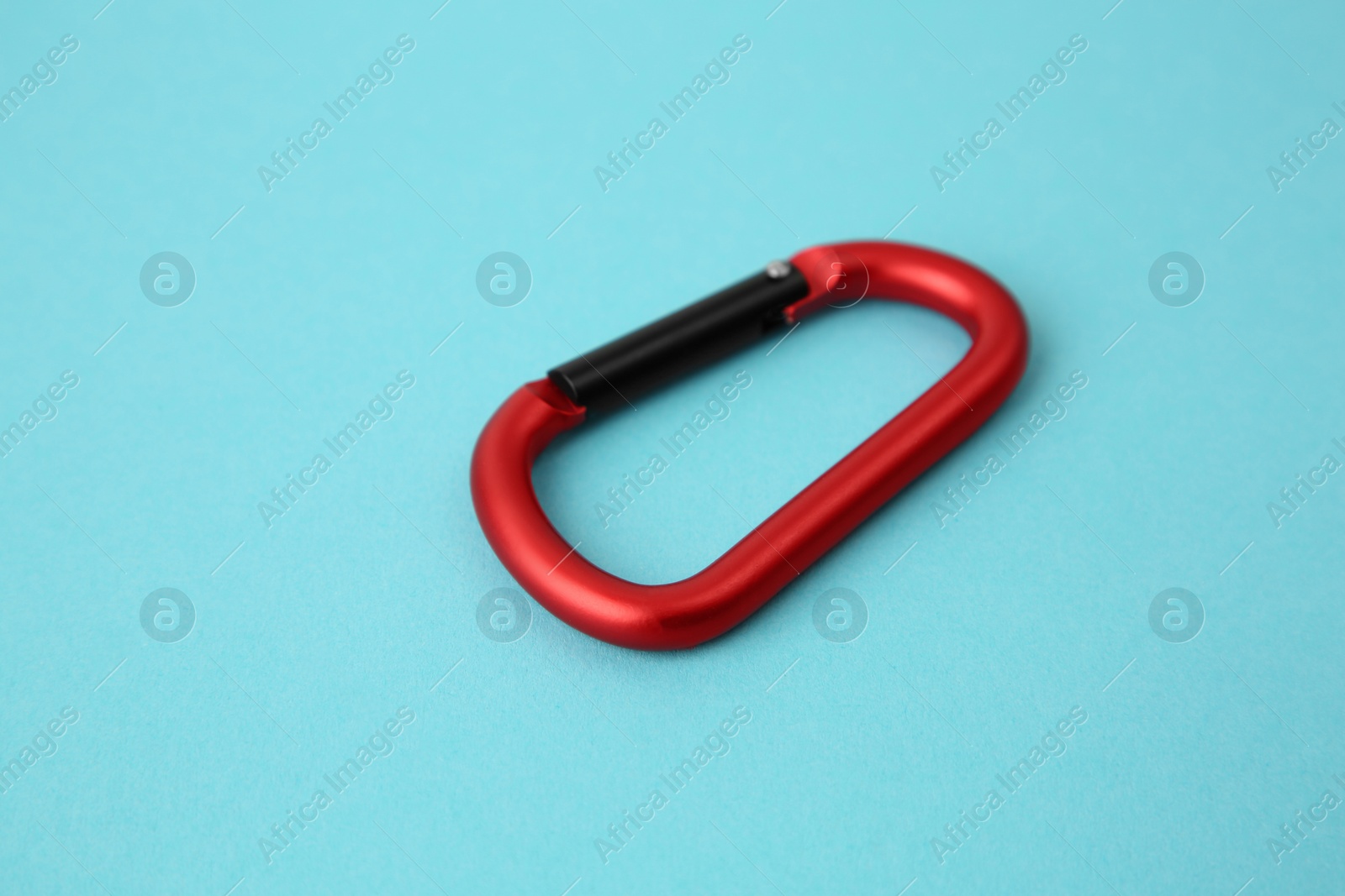 Photo of One red carabiner on light blue background, closeup