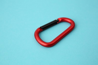 Photo of One red carabiner on light blue background, closeup