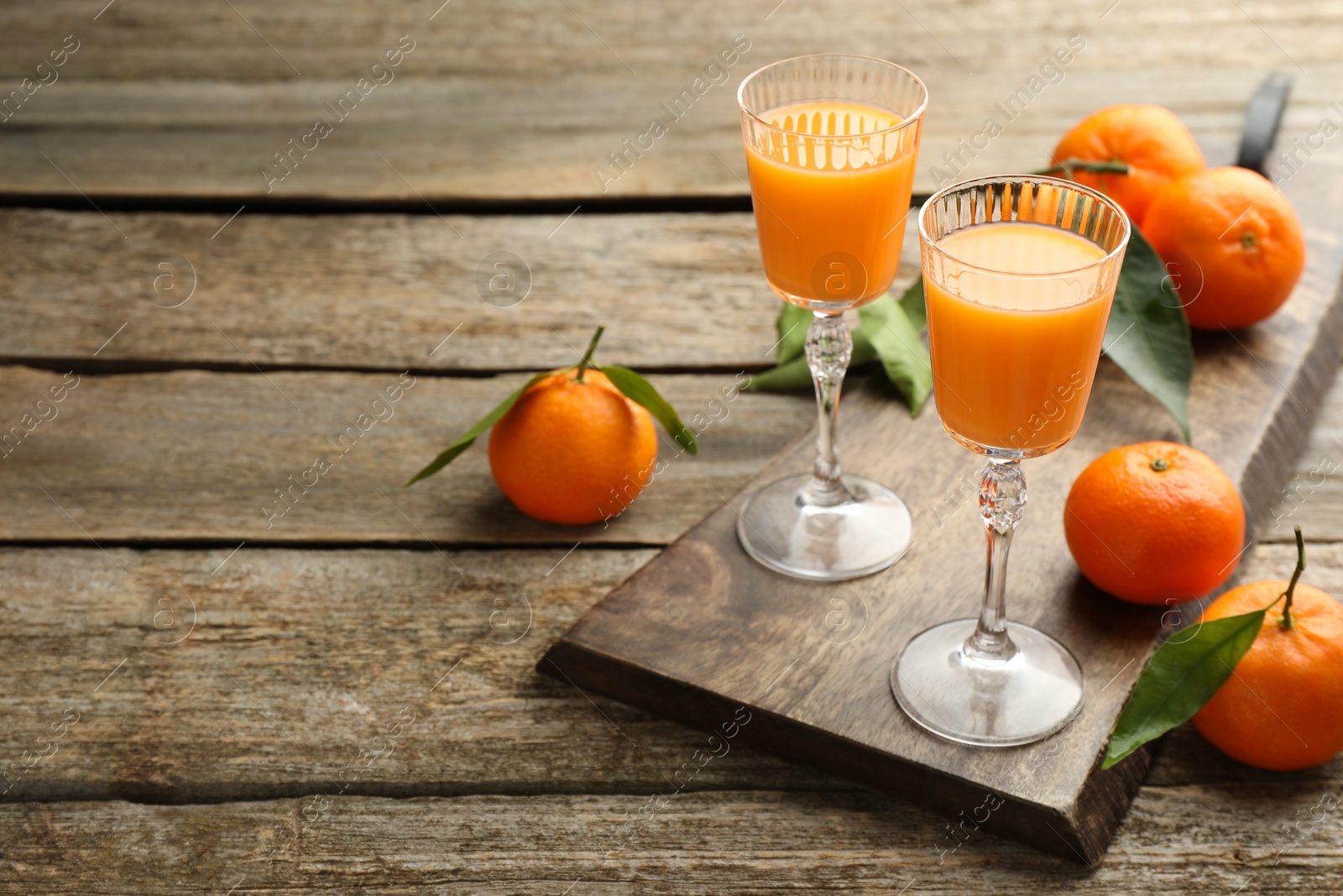 Photo of Delicious tangerine liqueur and fresh fruits on wooden table, space for text