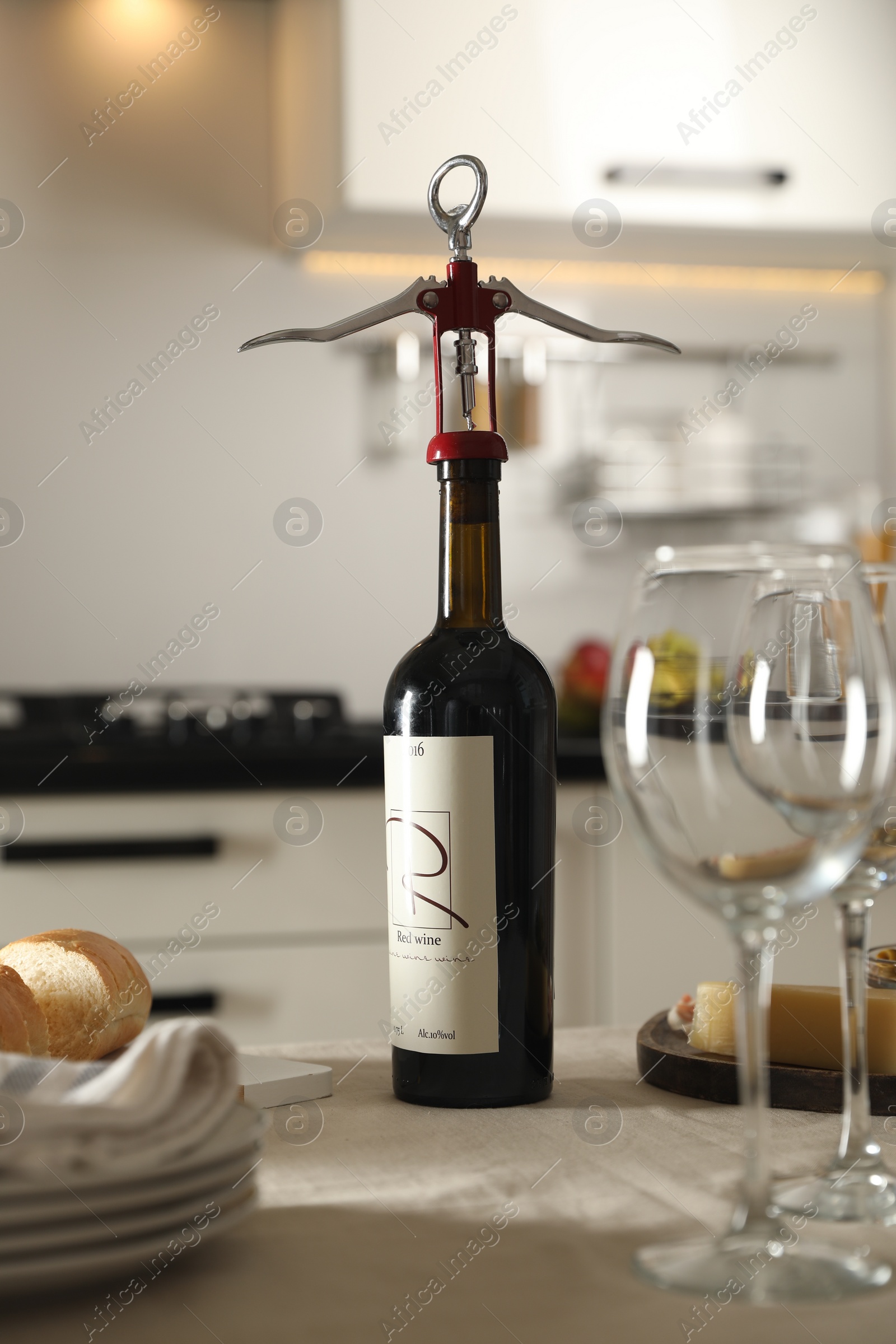 Photo of Wine bottle with corkscrew, wineglasses and food on table in kitchen