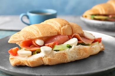 Photo of Tasty croissant sandwich with salmon on plate, closeup