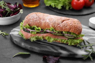 Photo of Delicious sandwich with fresh vegetables and salmon on black table