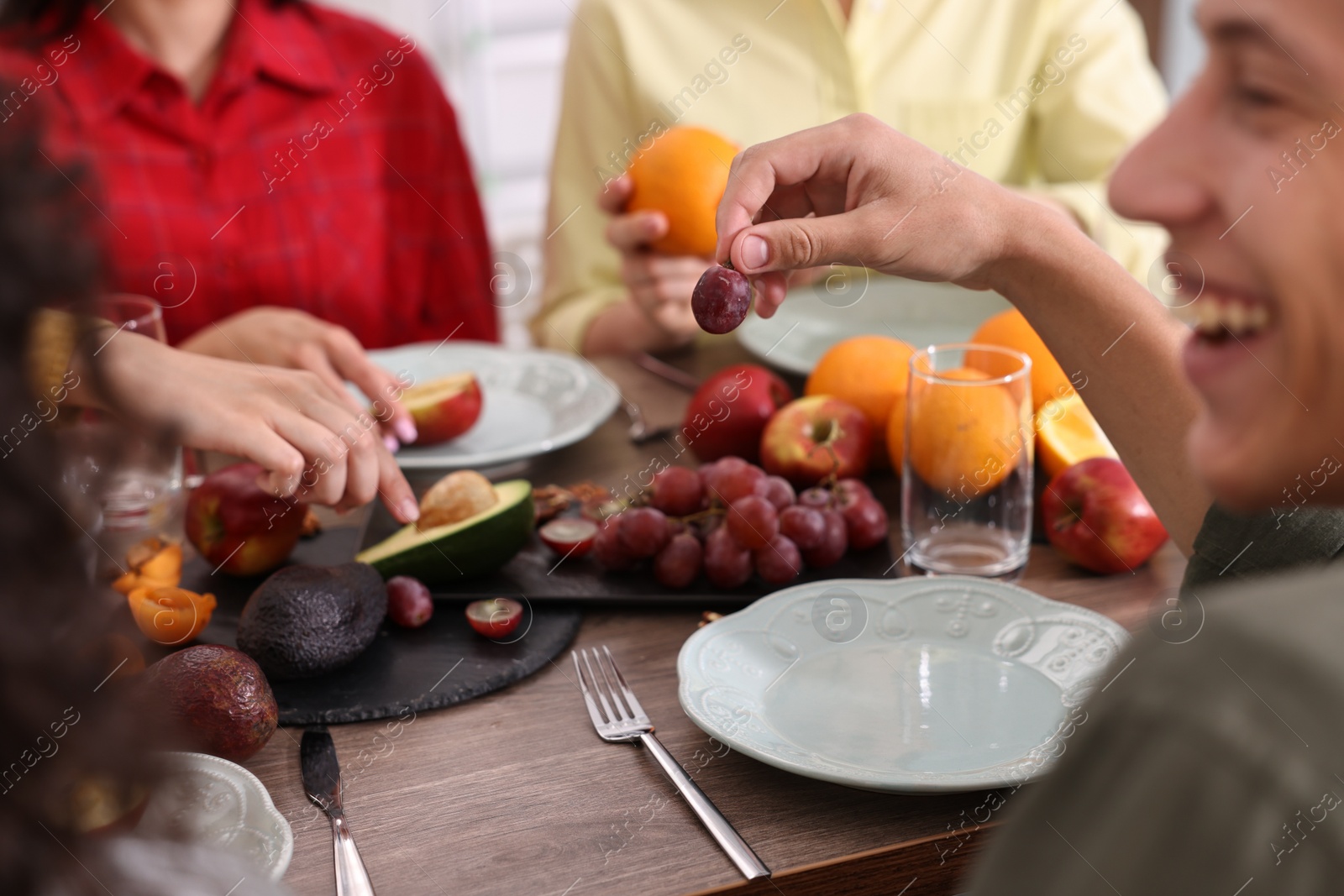 Photo of Vegetarian food. Friends eating fresh fruits at wooden table indoors, closeup