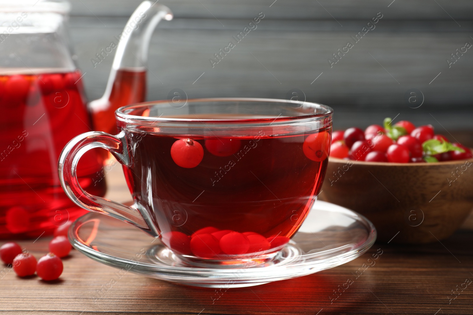 Photo of Tasty hot cranberry tea in glass cup and fresh berries on wooden table