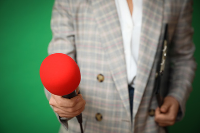 Journalist with microphone and clipboard on green background, closeup