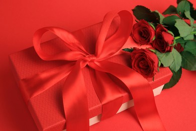 Photo of Beautiful gift box with bow and roses on red background