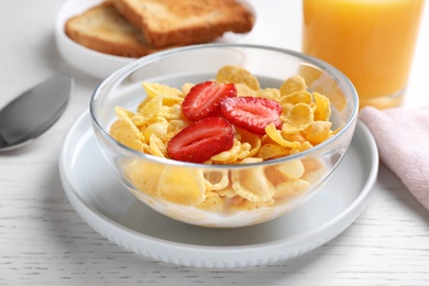 Photo of Tasty cornflakes with milk and strawberries on white wooden table, closeup. Healthy breakfast