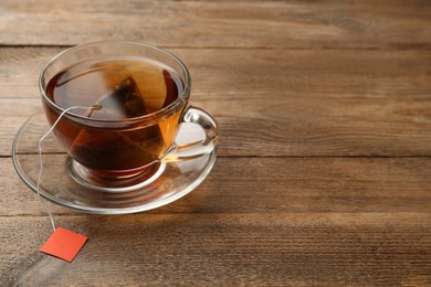 Photo of Tea bag in glass cup of hot water on wooden table. Space for text