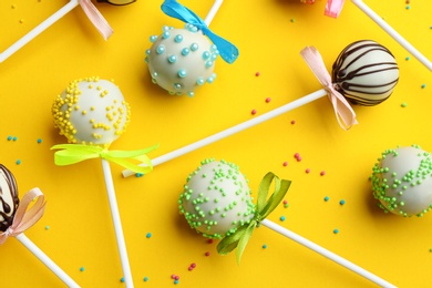 Different tasty cake pops with sprinkles on yellow background, flat lay