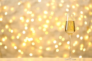 Photo of Glass of champagne on table against blurred lights. Space for text