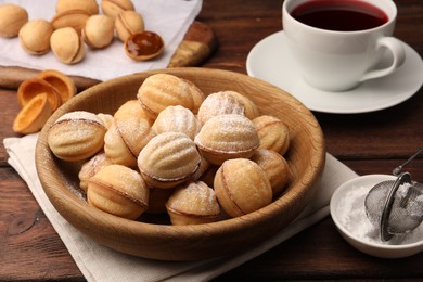 Photo of Delicious nut shaped cookies with boiled condensed milk and powdered sugar on wooden table, closeup