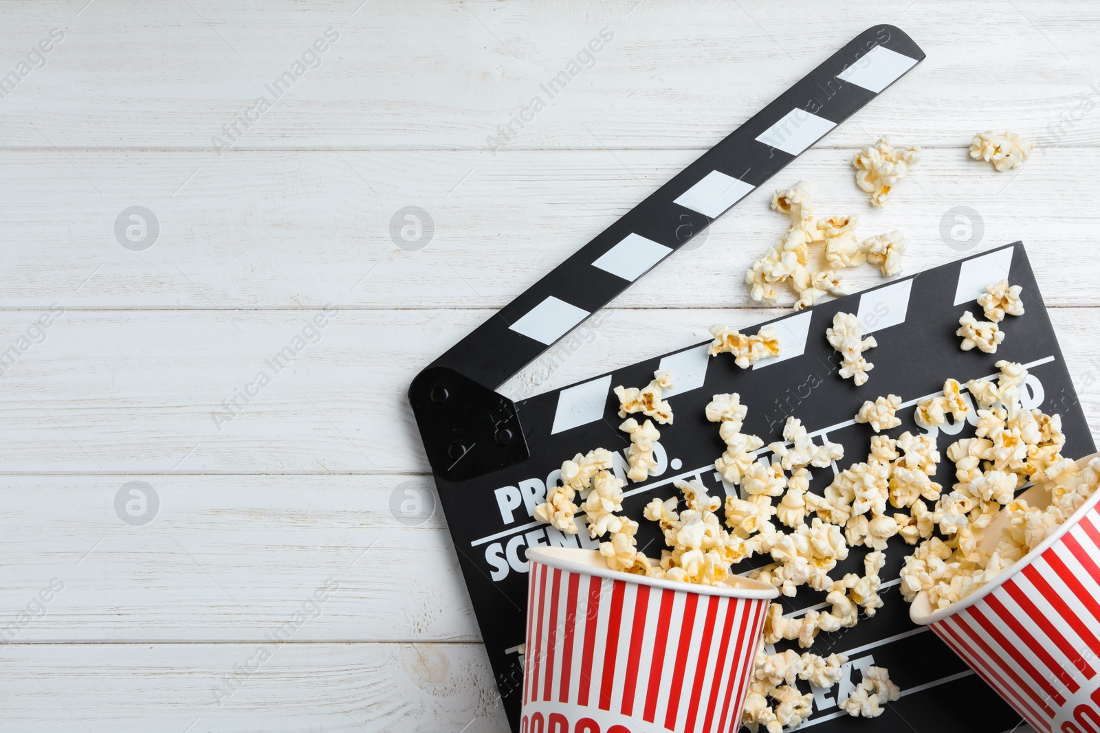 Photo of Clapperboard and popcorn on white wooden table, flat lay with space for text. Cinema snack