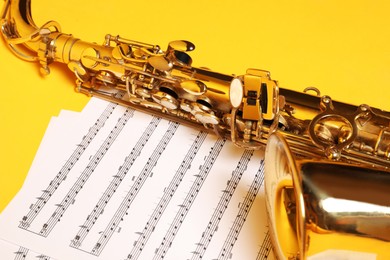 Photo of Beautiful saxophone and note sheets on yellow background, closeup