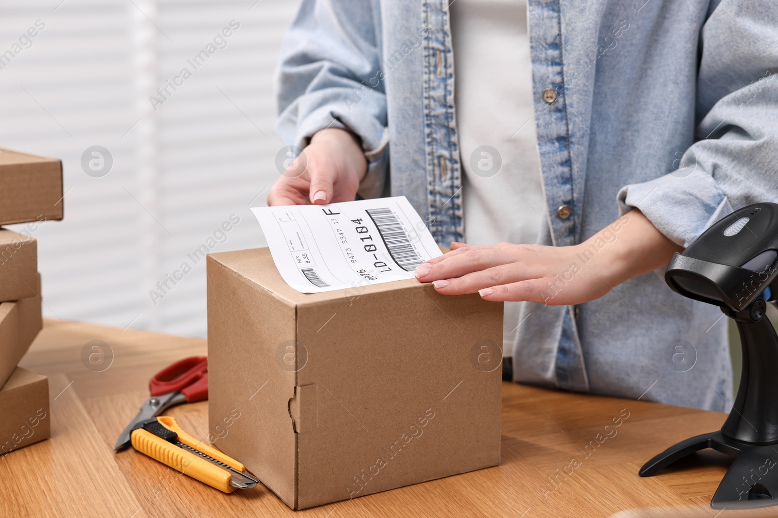 Photo of Parcel packing. Post office worker sticking barcode on box at wooden table indoors, closeup