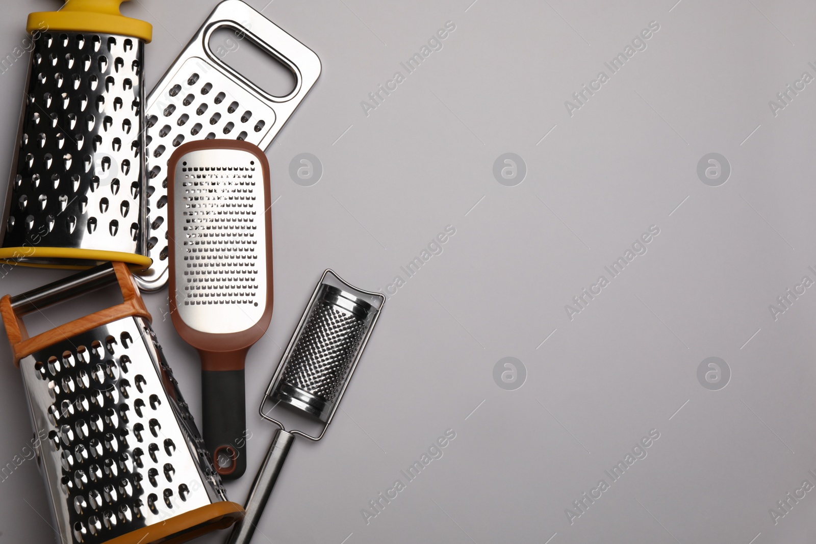 Photo of Different modern graters on grey background, flat lay. Space for text