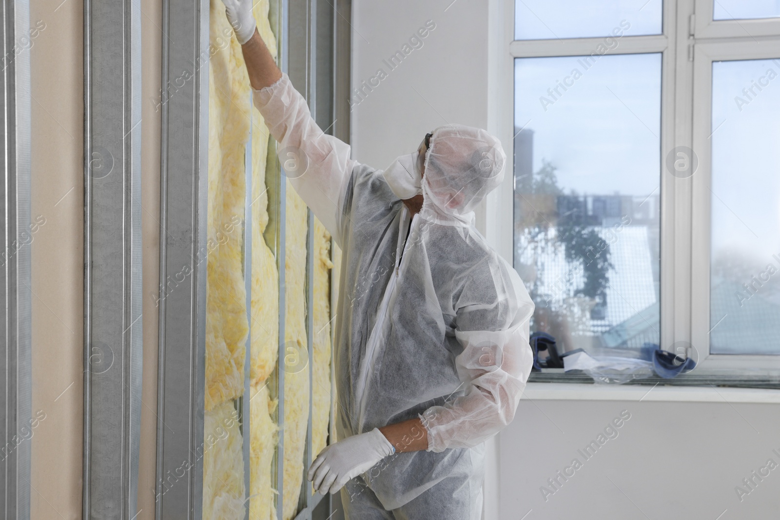 Photo of Worker in uniform and respiratory mask insulating wall indoors