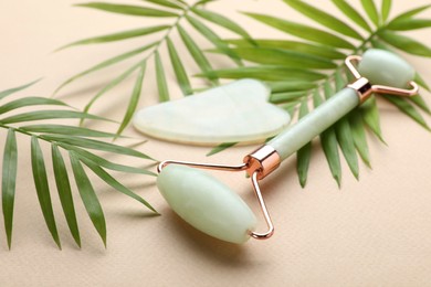 Gua sha stone, face roller and green leaves on beige background