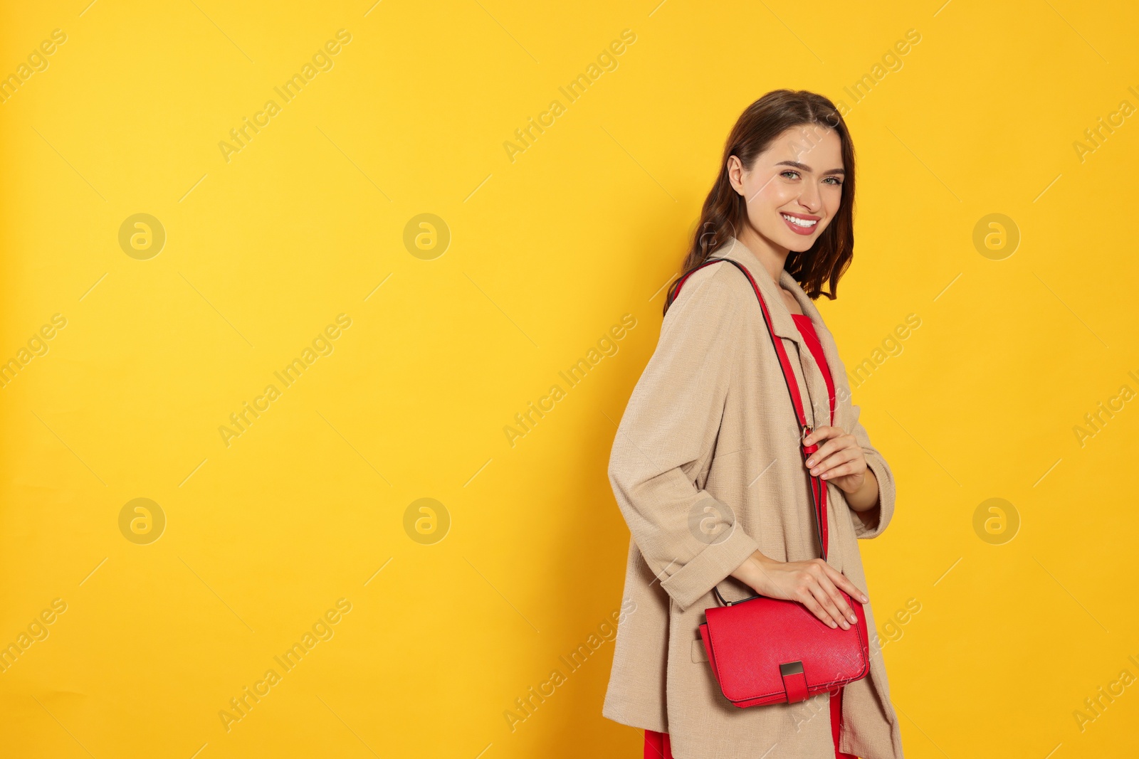 Photo of Beautiful young woman in fashionable outfit with stylish bag on yellow background, space for text