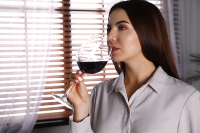 Photo of Beautiful young woman with glass of luxury red wine indoors. Space for text