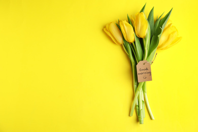 Photo of Beautiful tulips and GOOD MORNING wish on yellow background, top view. Space for text