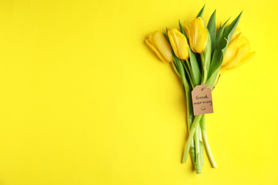 Beautiful tulips and GOOD MORNING wish on yellow background, top view. Space for text