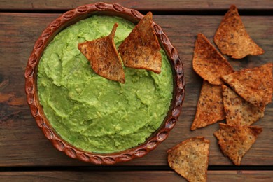 Photo of Delicious guacamole made of avocados and nachos on wooden table, flat lay