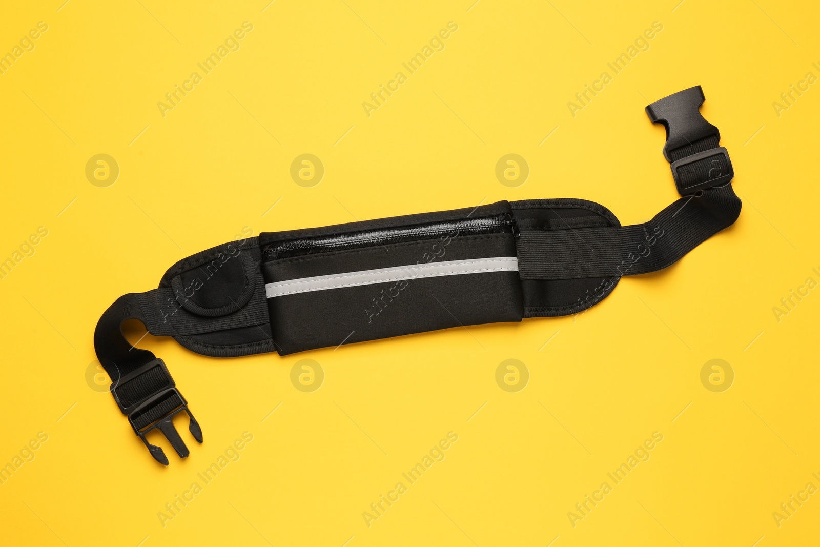 Photo of Stylish black waist bag on yellow background, top view