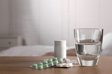 Glass of water, different pills in blisters and medical bottle on wooden table indoors, space for text