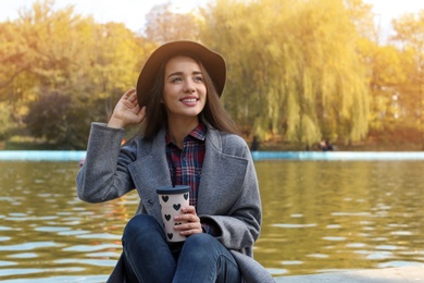 Portrait of young beautiful woman with drink in park. Autumn walk