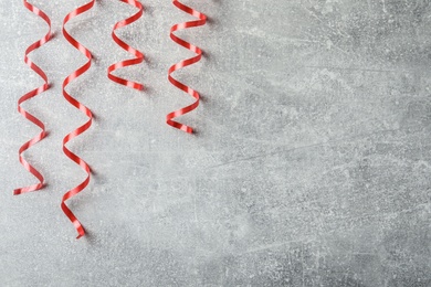 Photo of Shiny red serpentine streamers on grey background, flat lay. Space for text