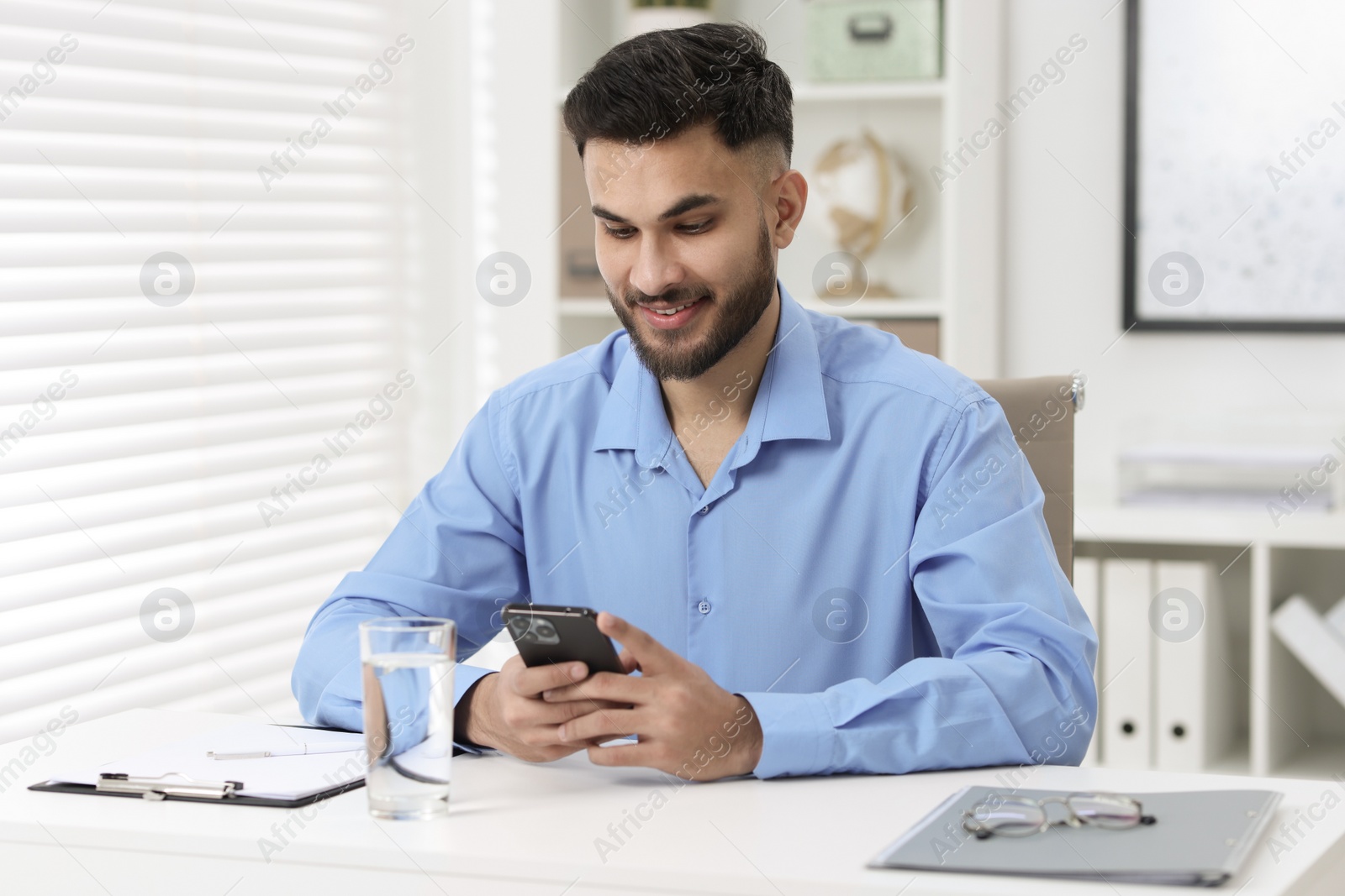 Photo of Handsome young man using smartphone at white table in office
