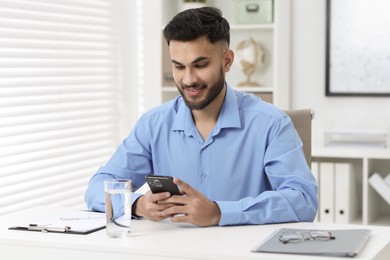 Handsome young man using smartphone at white table in office