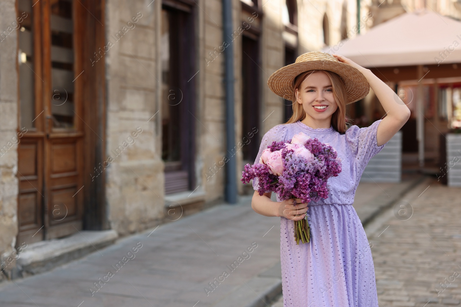 Photo of Beautiful woman with bouquet of spring flowers on city street, space for text