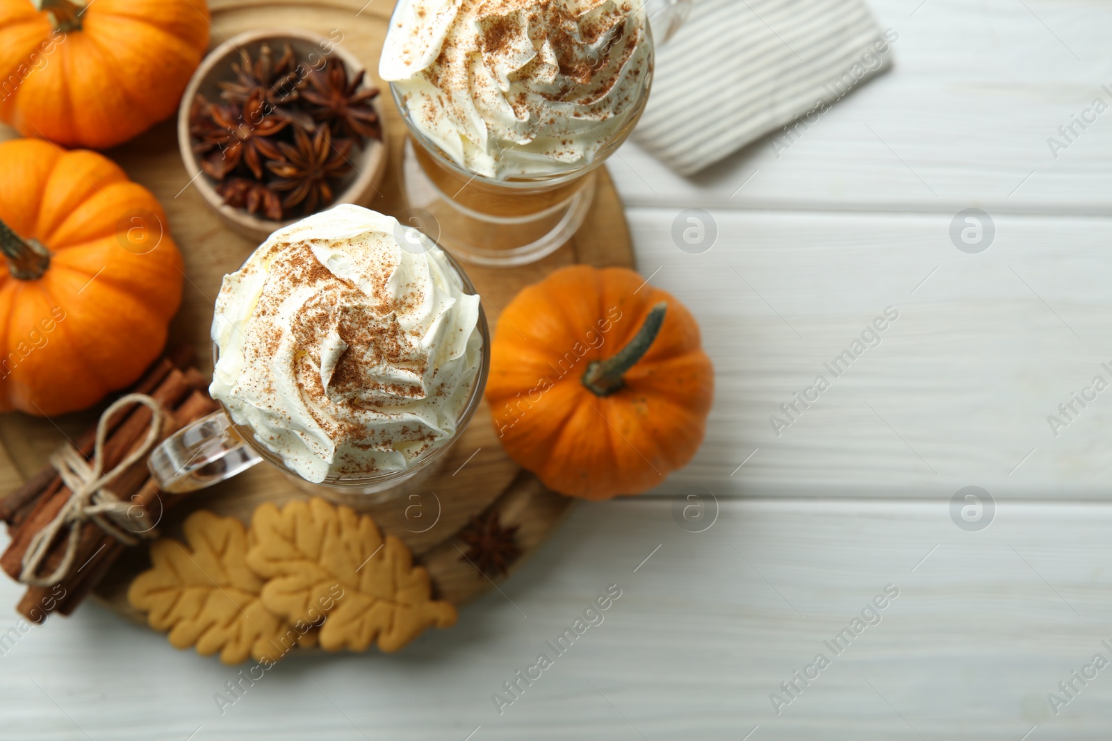 Photo of Tasty pumpkin latte with whipped cream in glasses, spices and cookies on white wooden table, top view. Space for text