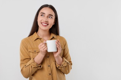 Happy young woman holding white ceramic mug on light grey background, space for text