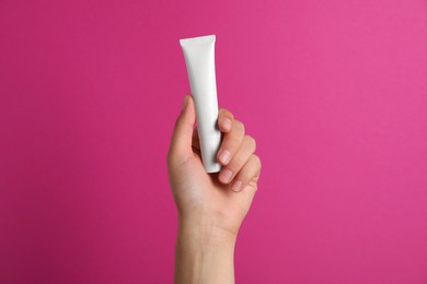 Photo of Woman holding tube of face cream on pink background, closeup