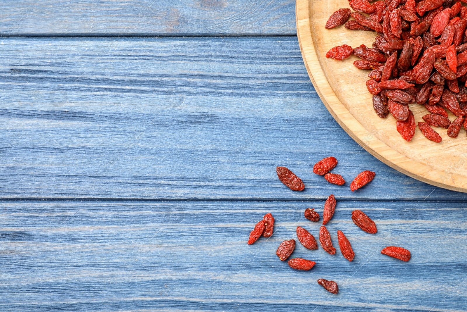 Photo of Dried goji berries on blue wooden table, flat lay. Space for text