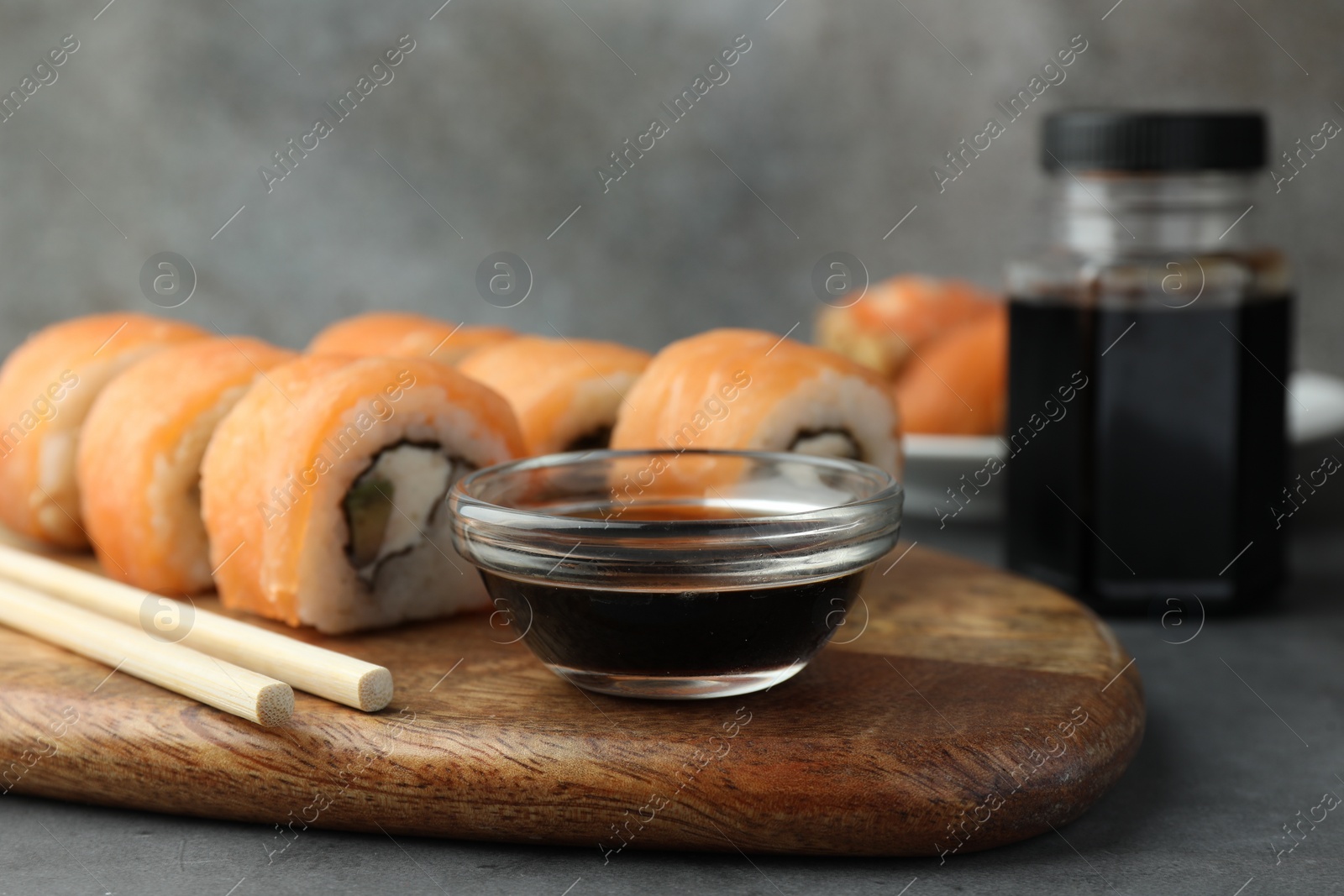 Photo of Tasty soy sauce, chopsticks and sushi rolls with salmon on grey table