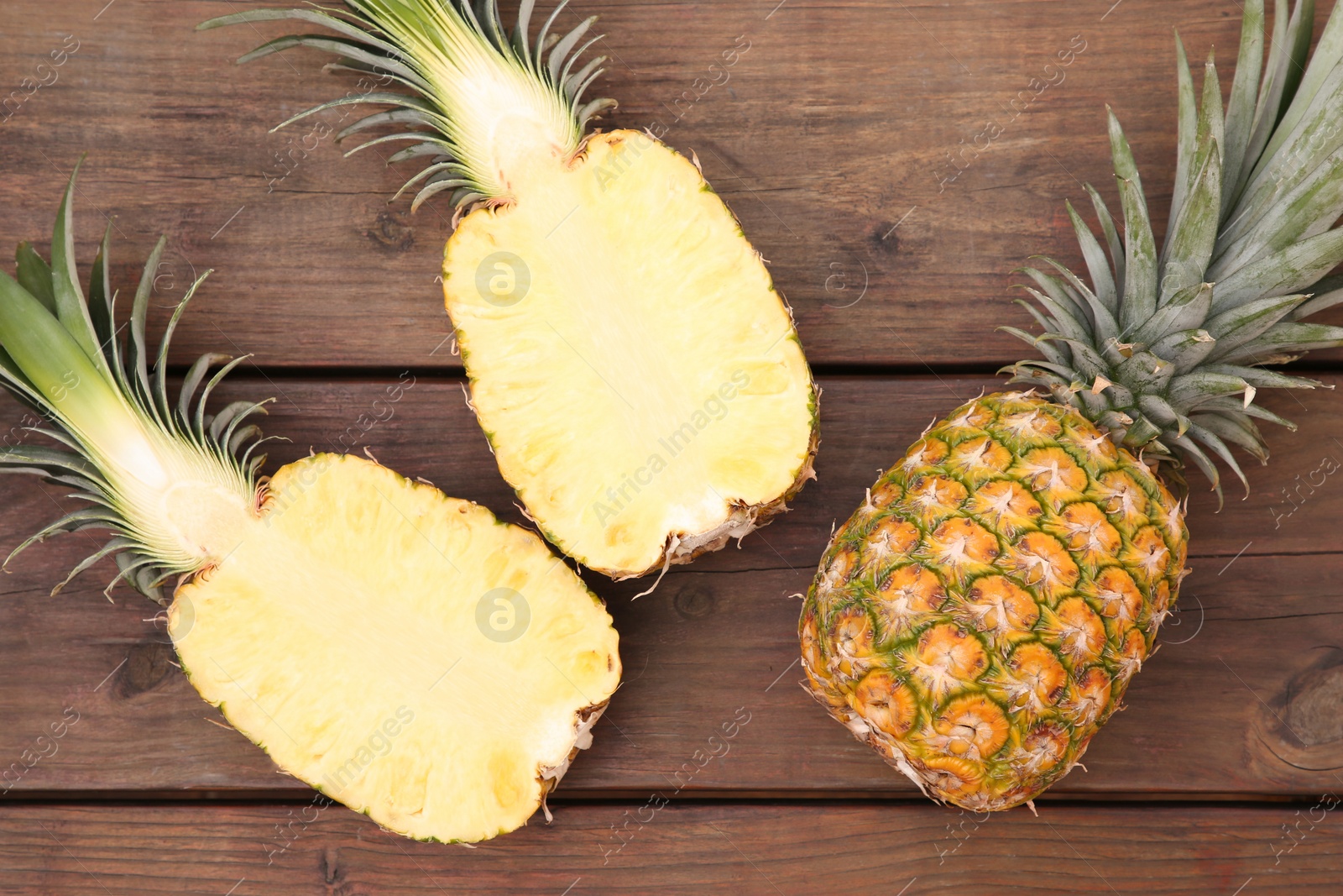 Photo of Whole and cut ripe pineapples on wooden table, flat lay