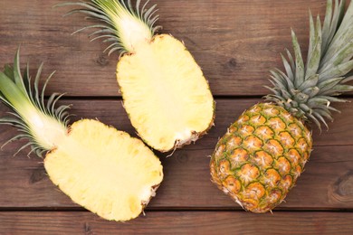 Whole and cut ripe pineapples on wooden table, flat lay